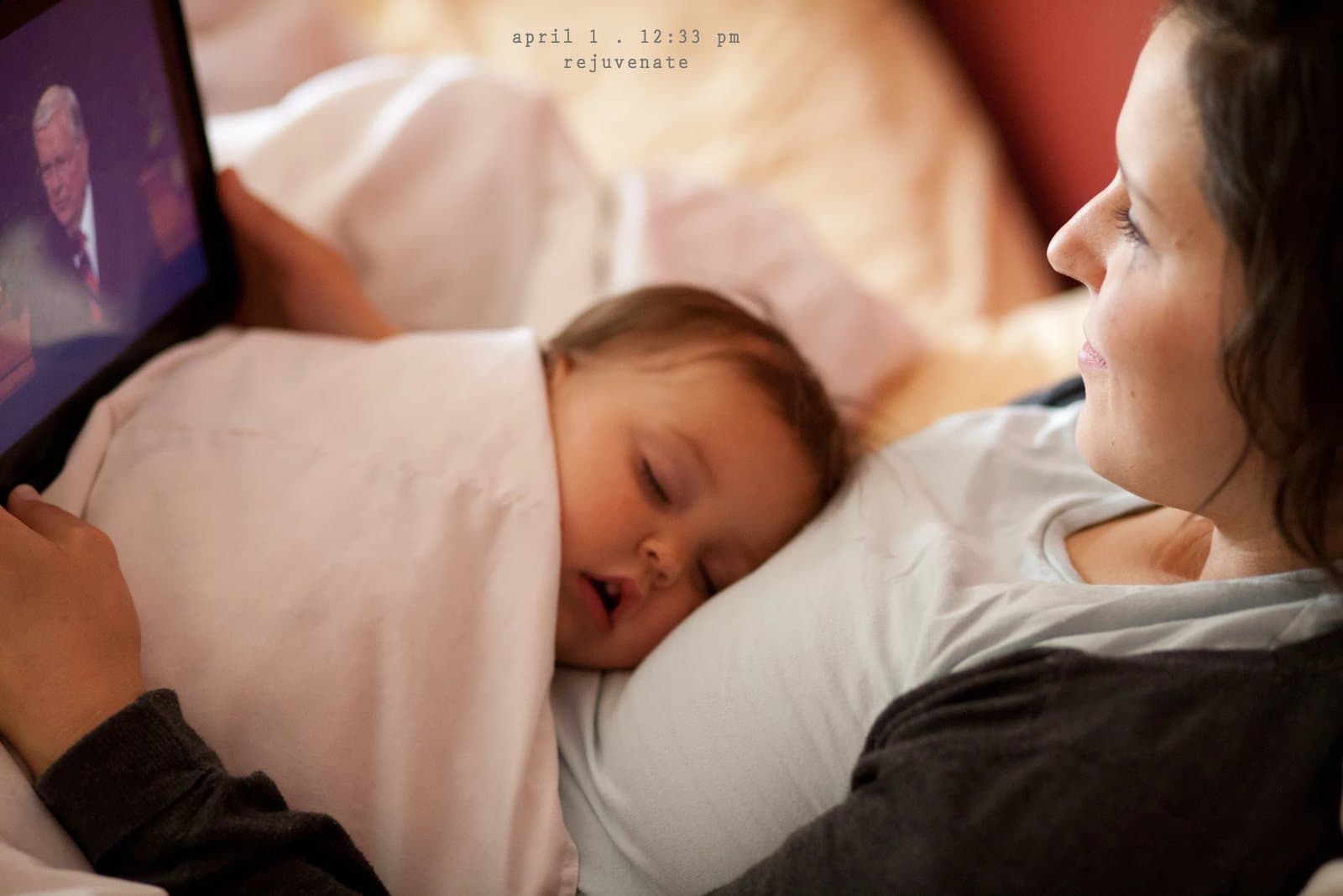 A baby sleeps on a pillow beside a woman watching a tablet in bed, captioned rejuvenate.