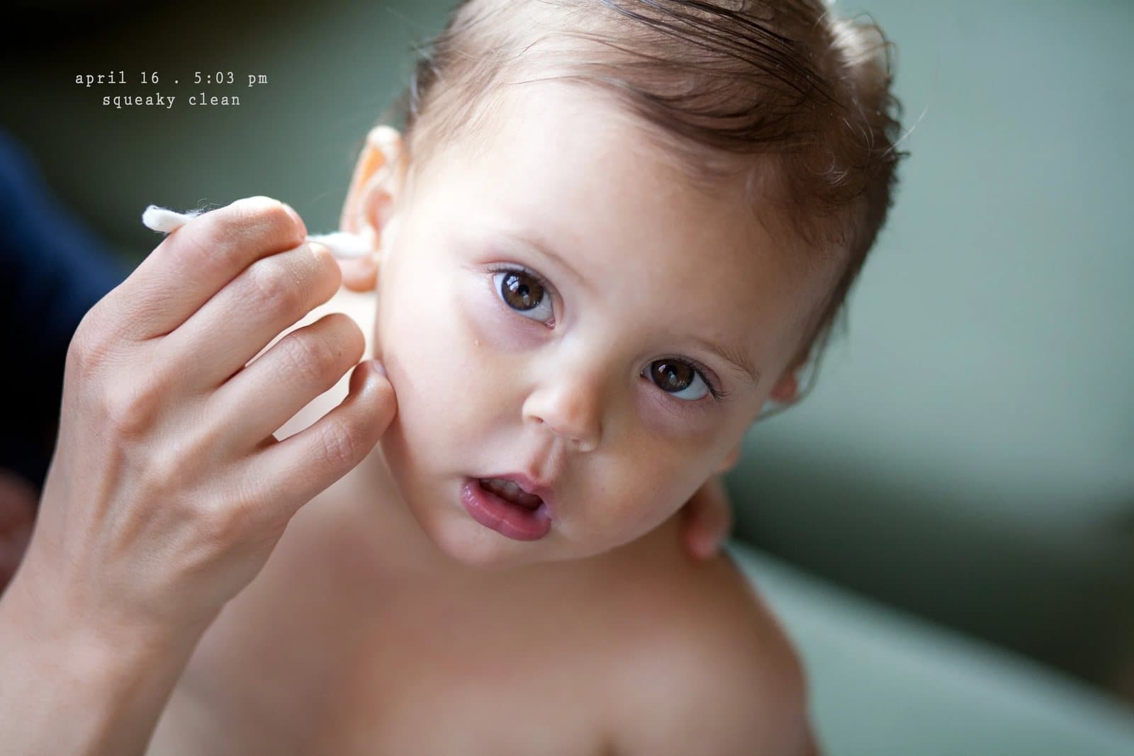 A baby looks up while an adult cleans her ear with a cotton swab, captioned squeaky clean.