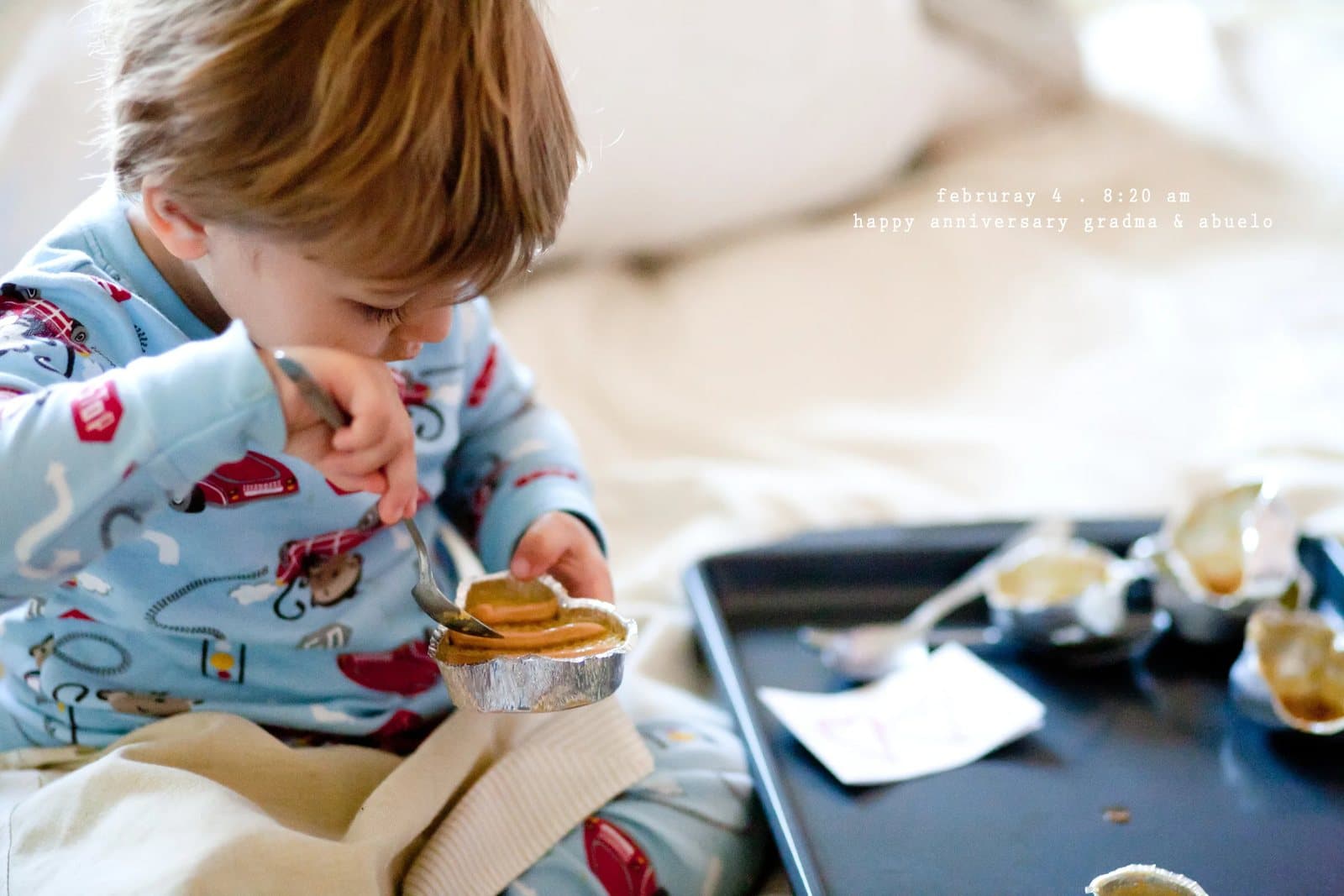 A toddler in pajamas eats a cupcake from a baking tray, captioned happy anniversary grandma and abuelo.
