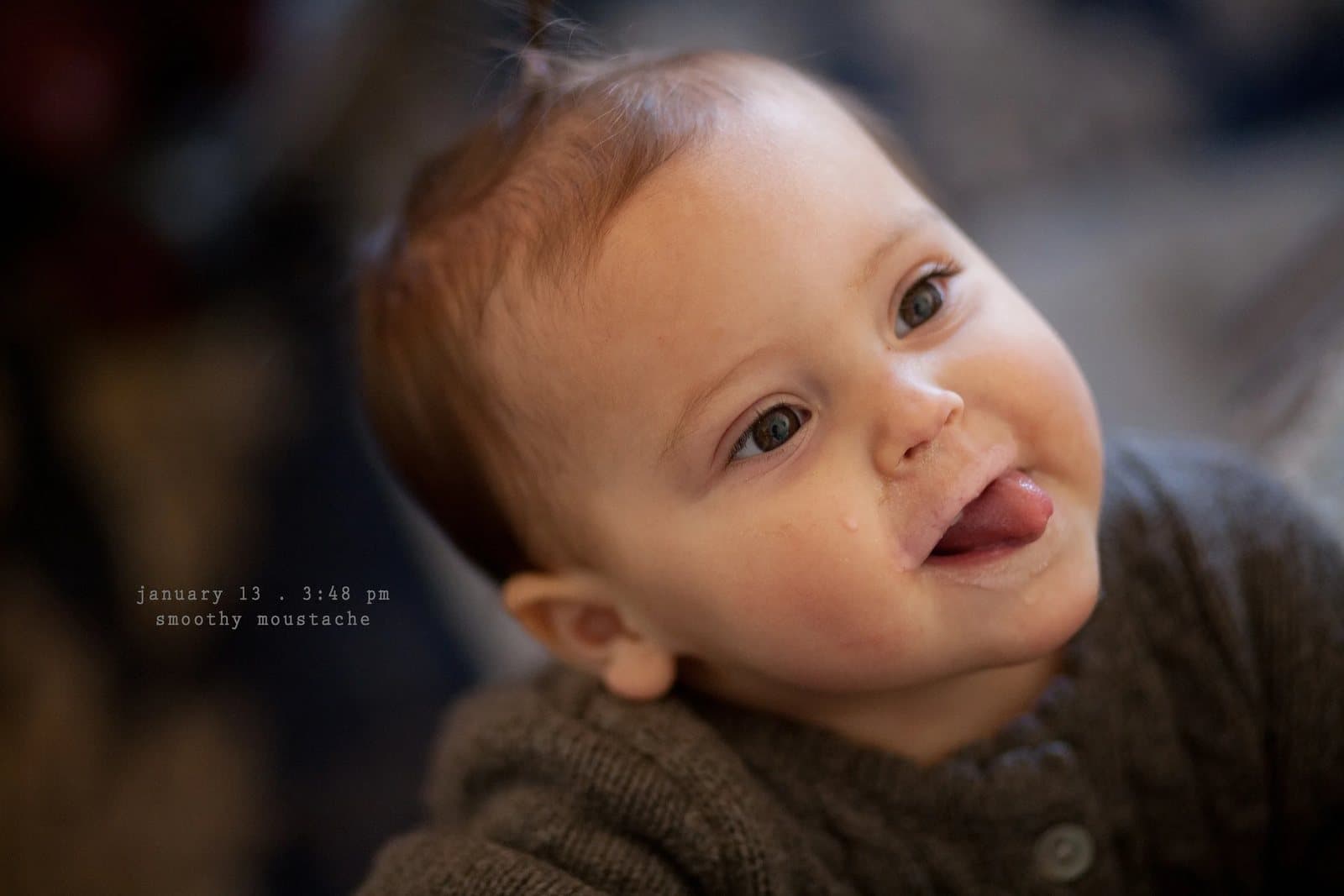 A baby sticks out his tongue with a smudge above his lip, captioned smoothy moustache.