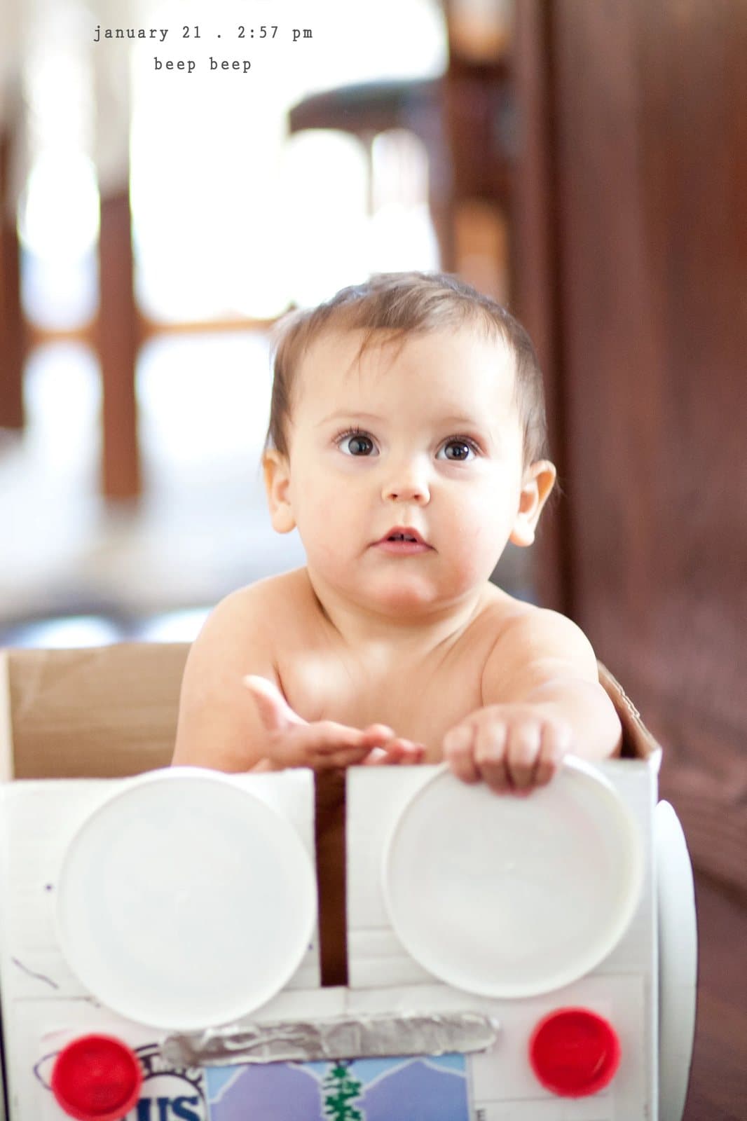 A baby sits in a cardboard box car with plate headlights, captioned beep beep.
