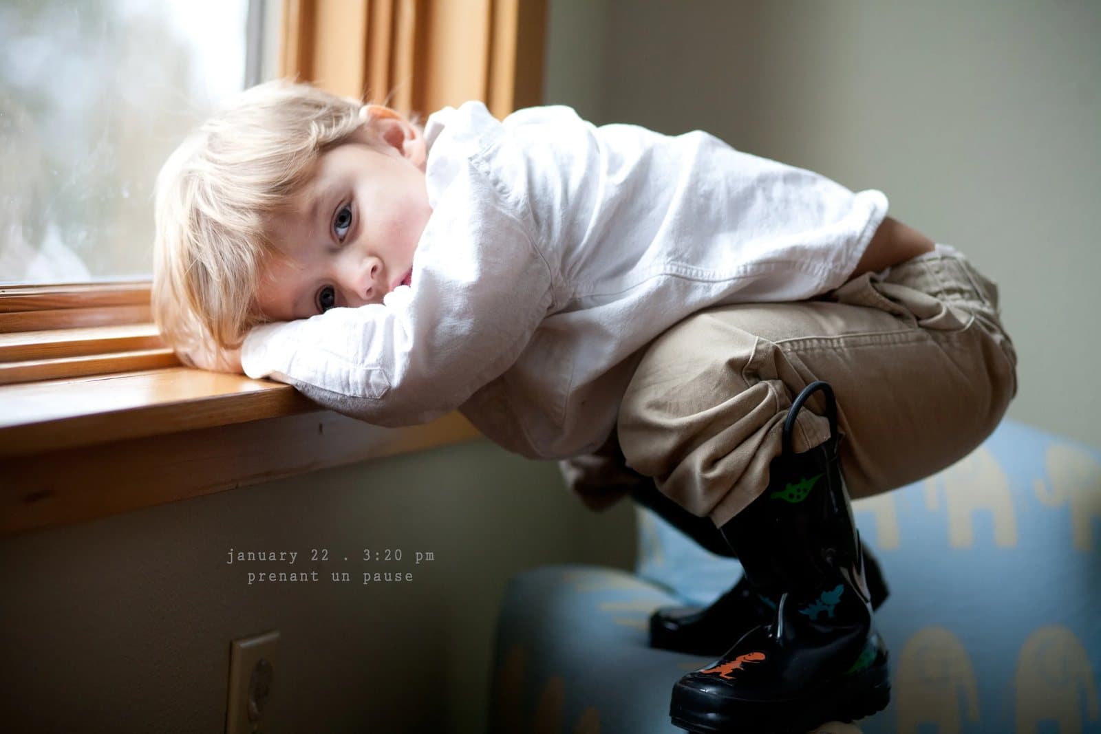 A toddler in rain boots leans on a windowsill, captioned prenant un pause.