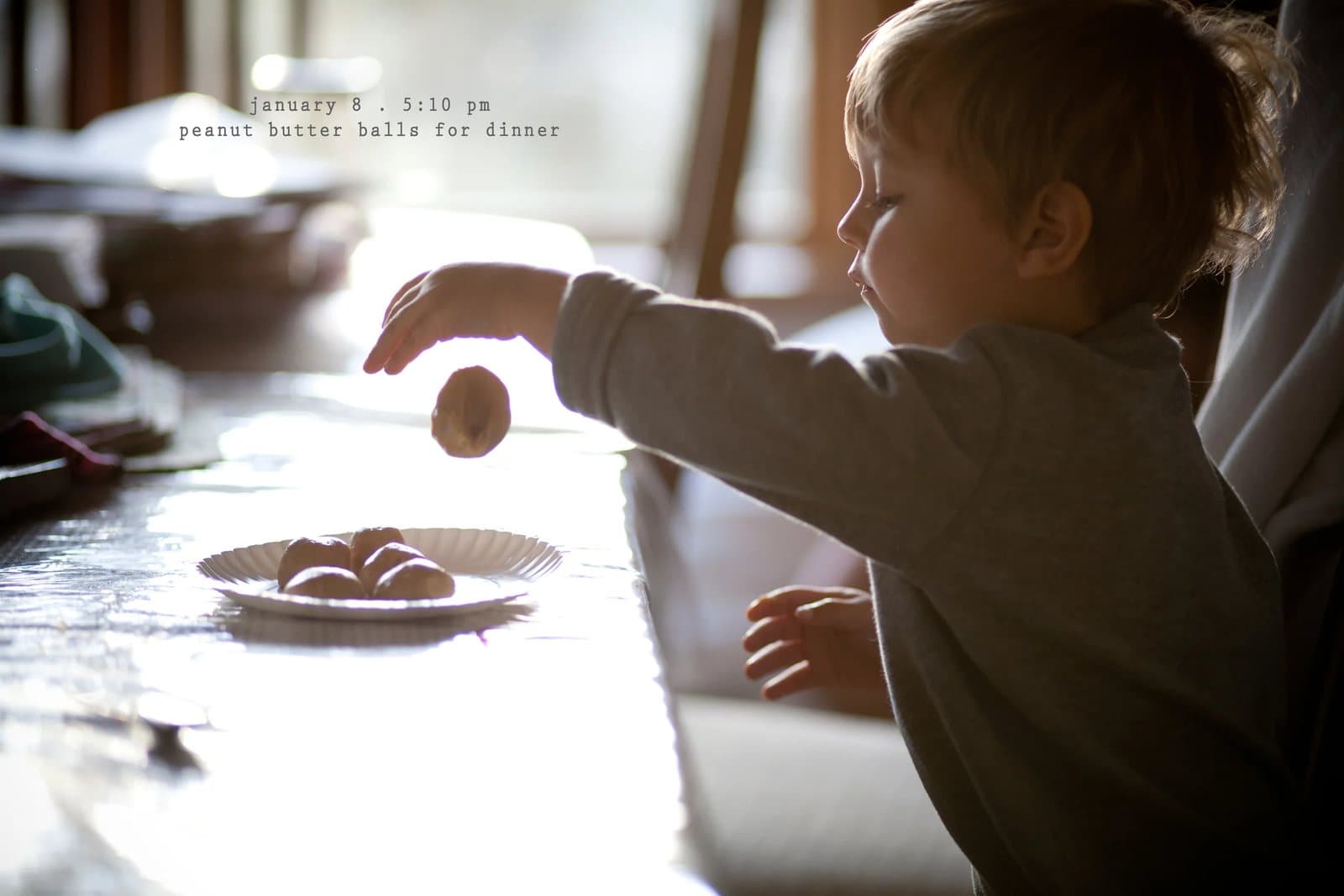 A toddler reaches for peanut butter balls on a plate, captioned peanut butter balls for dinner.