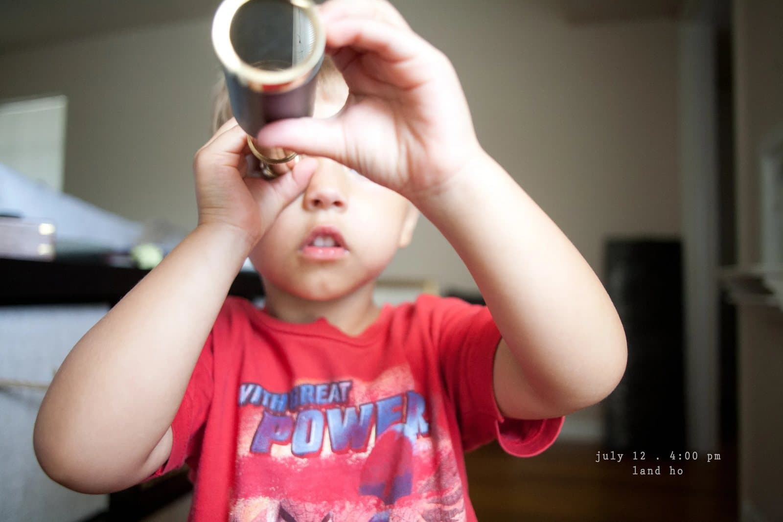A boy in a red shirt peers through a small brass telescope, captioned land ho.