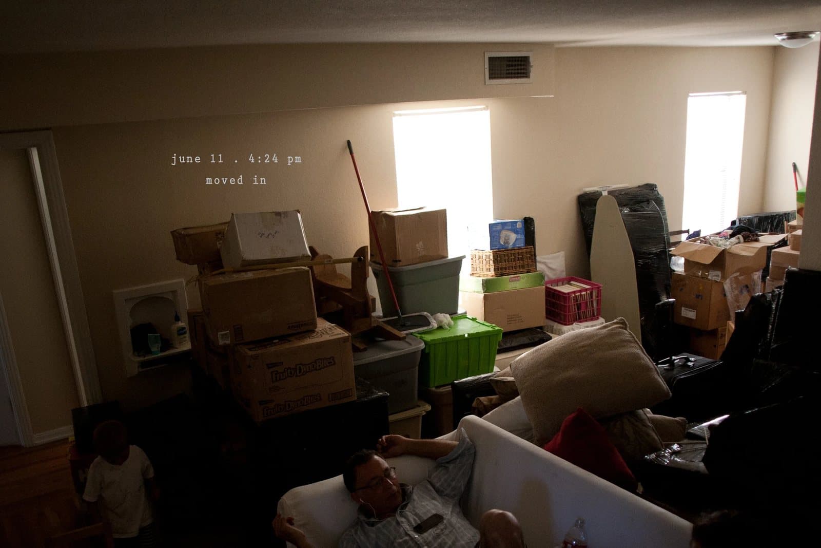 A living room stacked with moving boxes, a man resting on a couch, captioned moved in.
