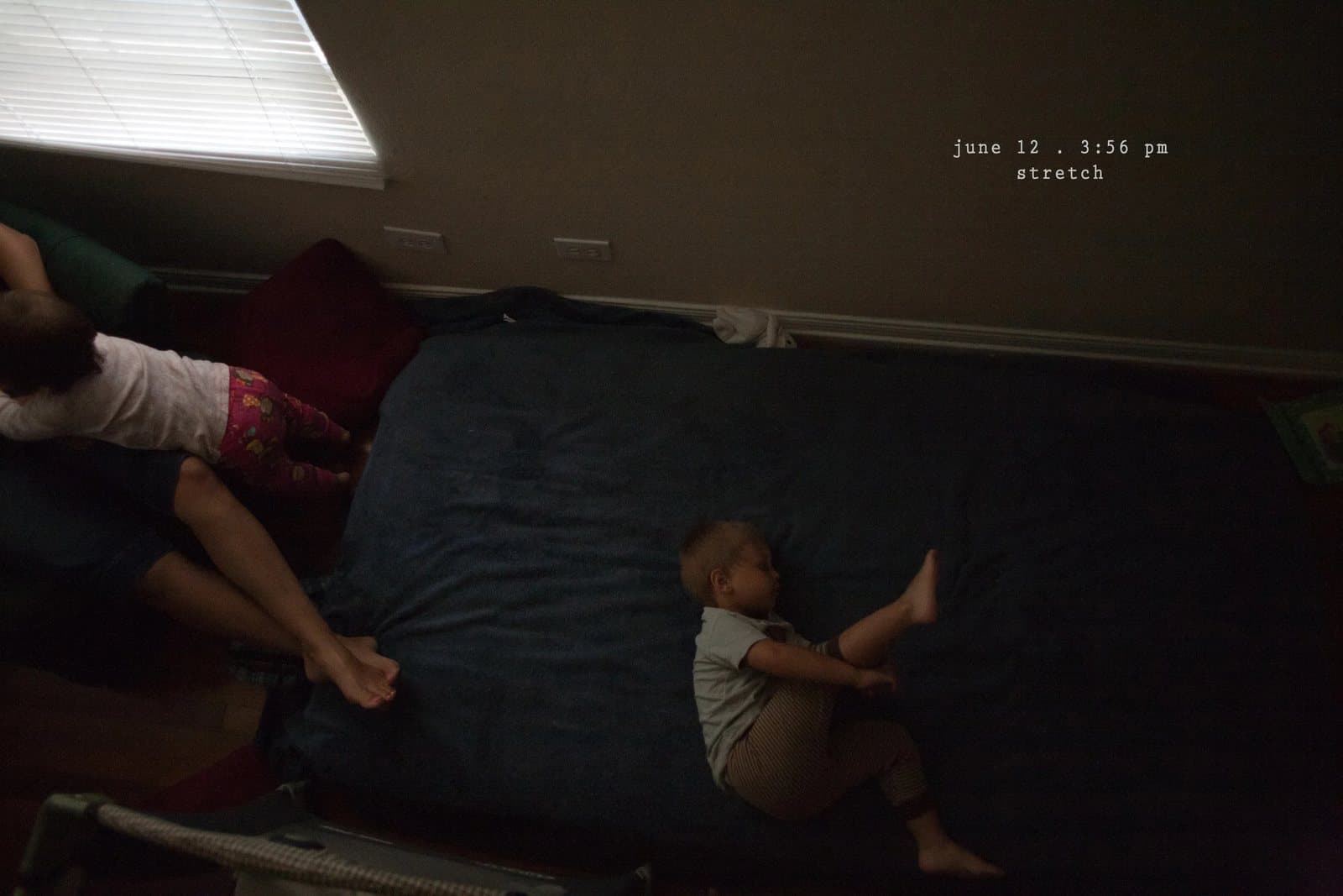A woman and a baby stretch on a mattress in a dim room, captioned stretch.