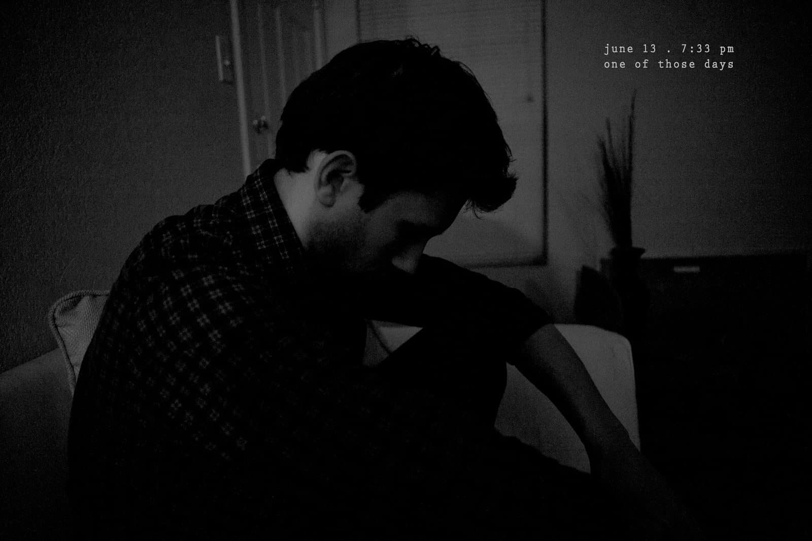 A man sits hunched in shadow with his head bowed, captioned one of those days.