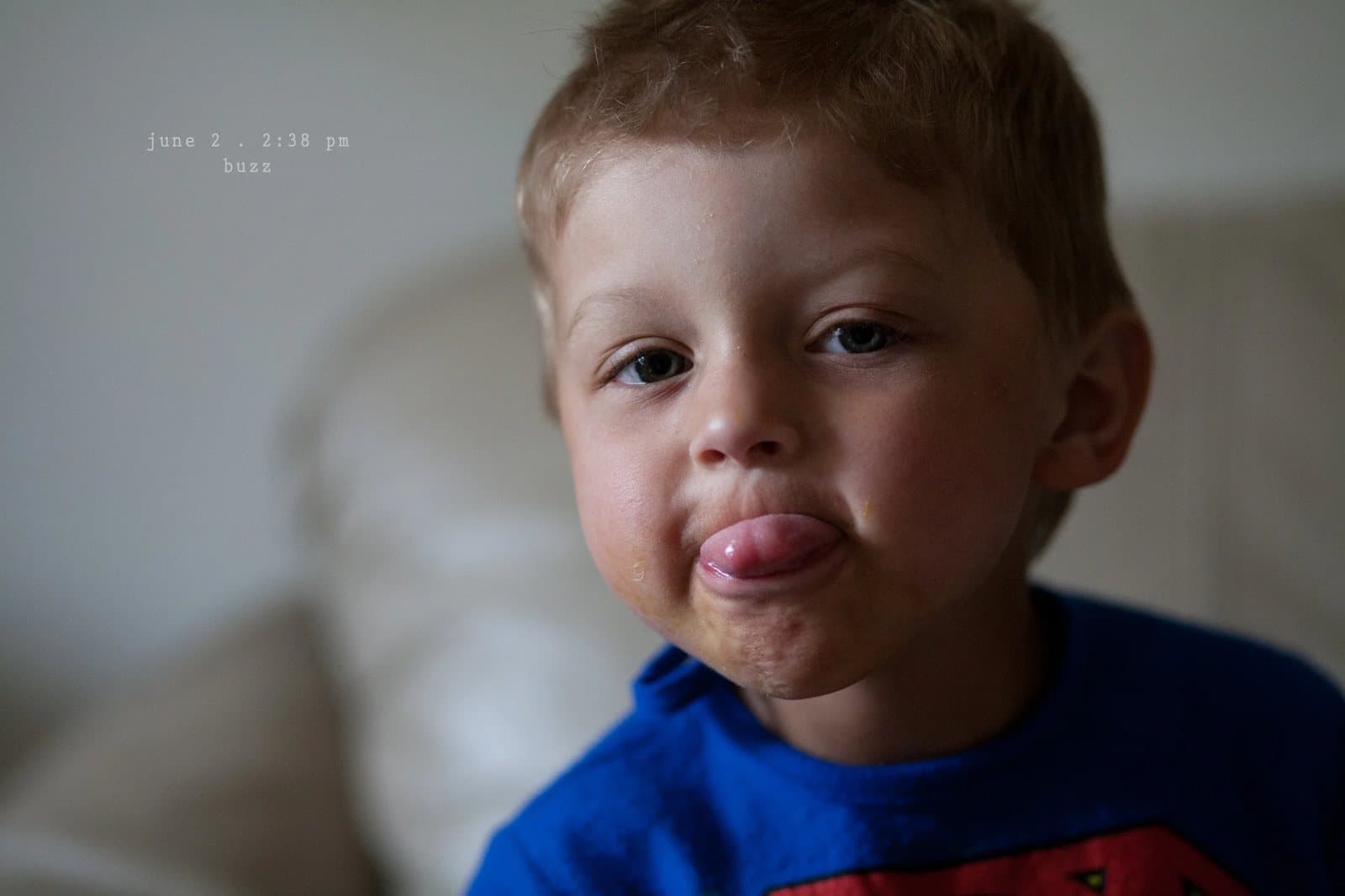 A toddler in a blue shirt sticks out his tongue at the camera.