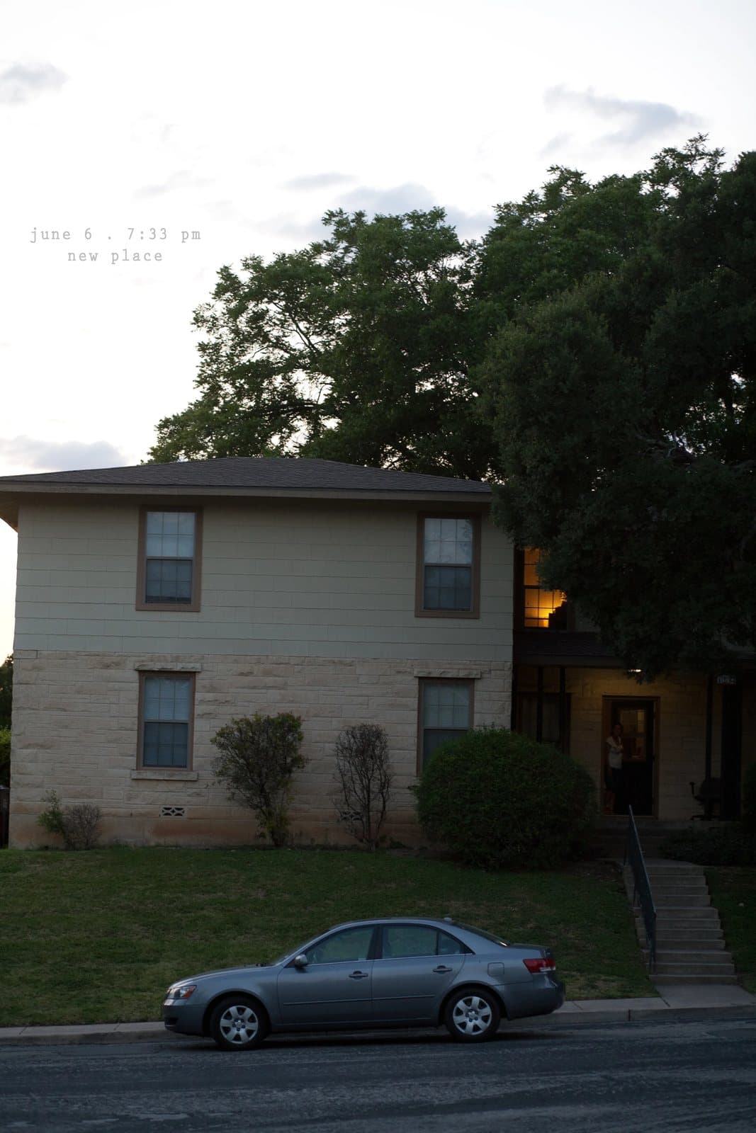 A two-story duplex with a gray sedan parked out front at dusk, captioned new place.