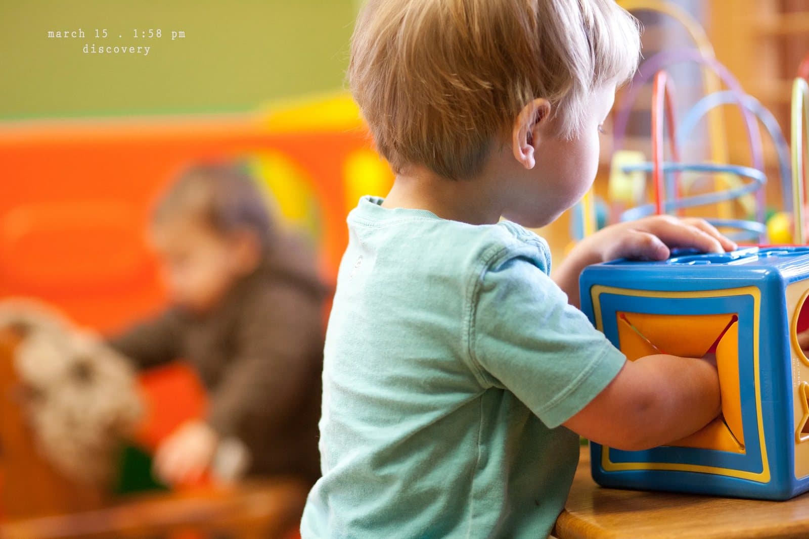 A toddler plays with a bead maze toy cube, captioned discovery.