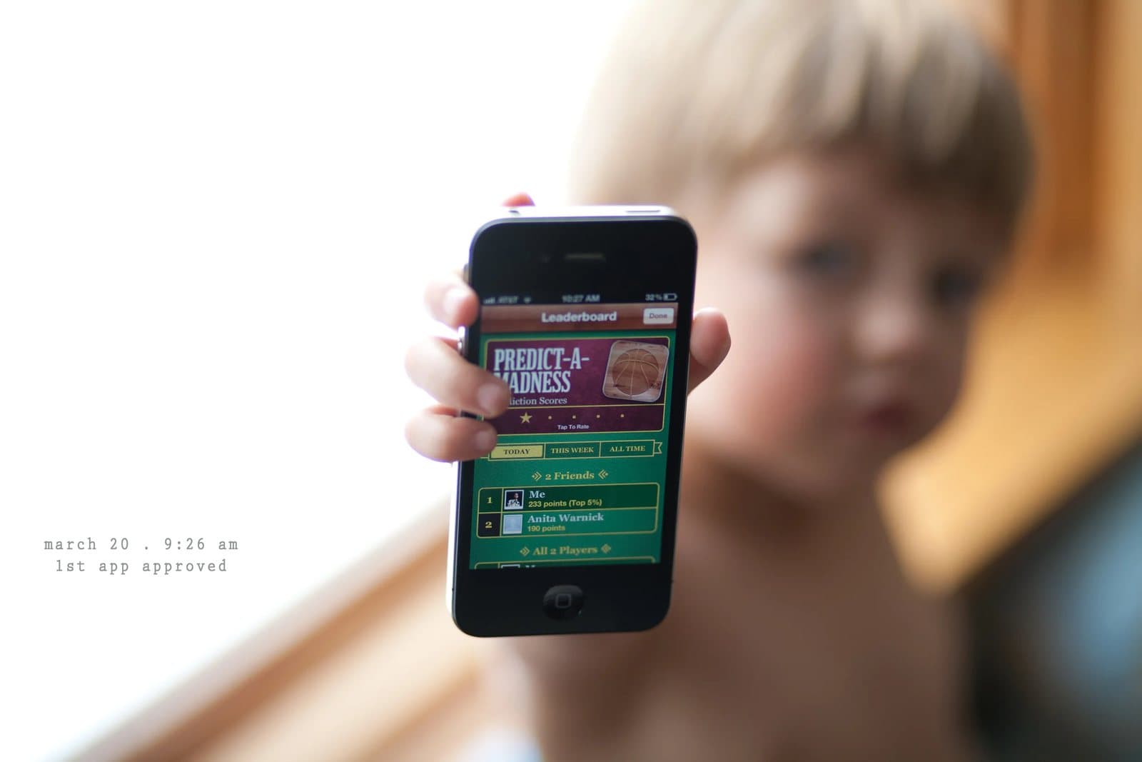 A boy holds up a phone showing the Predict-A-Madness app, captioned 1st app approved.