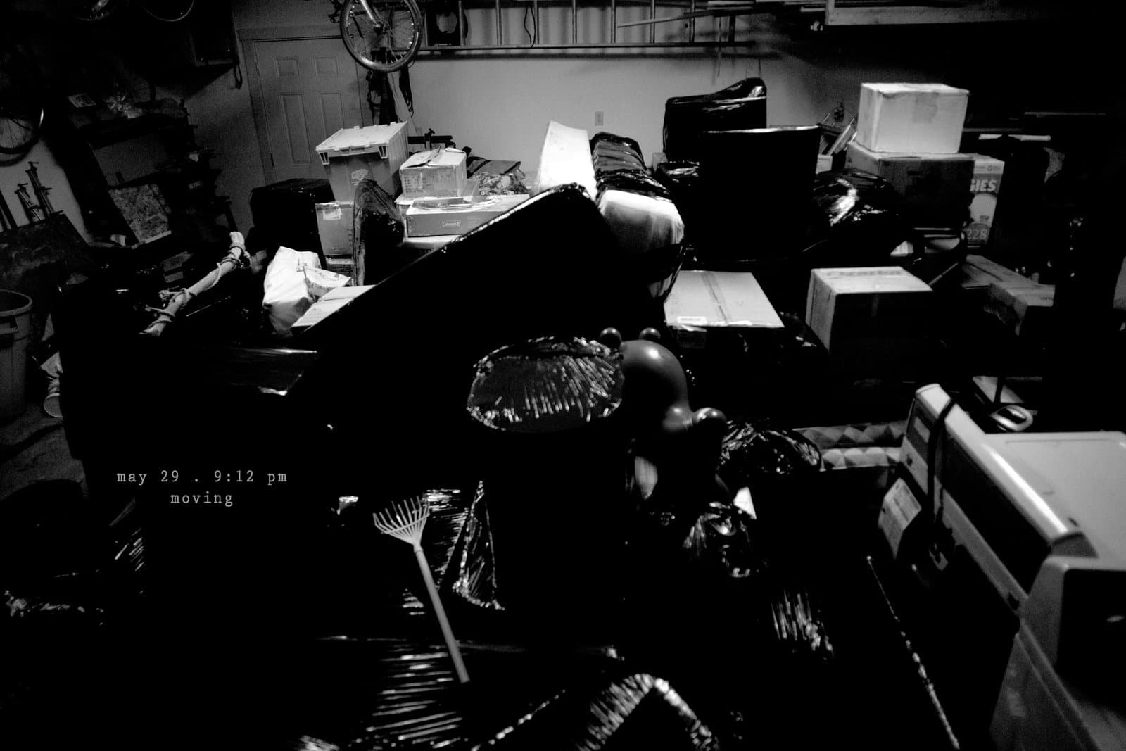 A garage crammed with boxes and furniture in black and white, captioned moving.