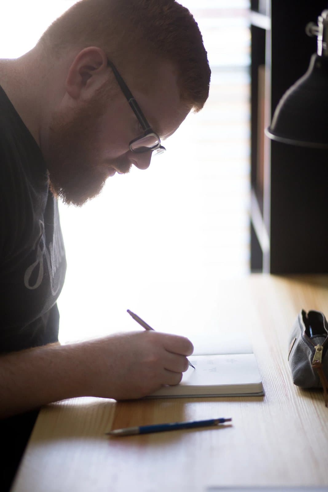 Kyle sketches in a notebook by a bright window, showing the light, airy feel of his brand.