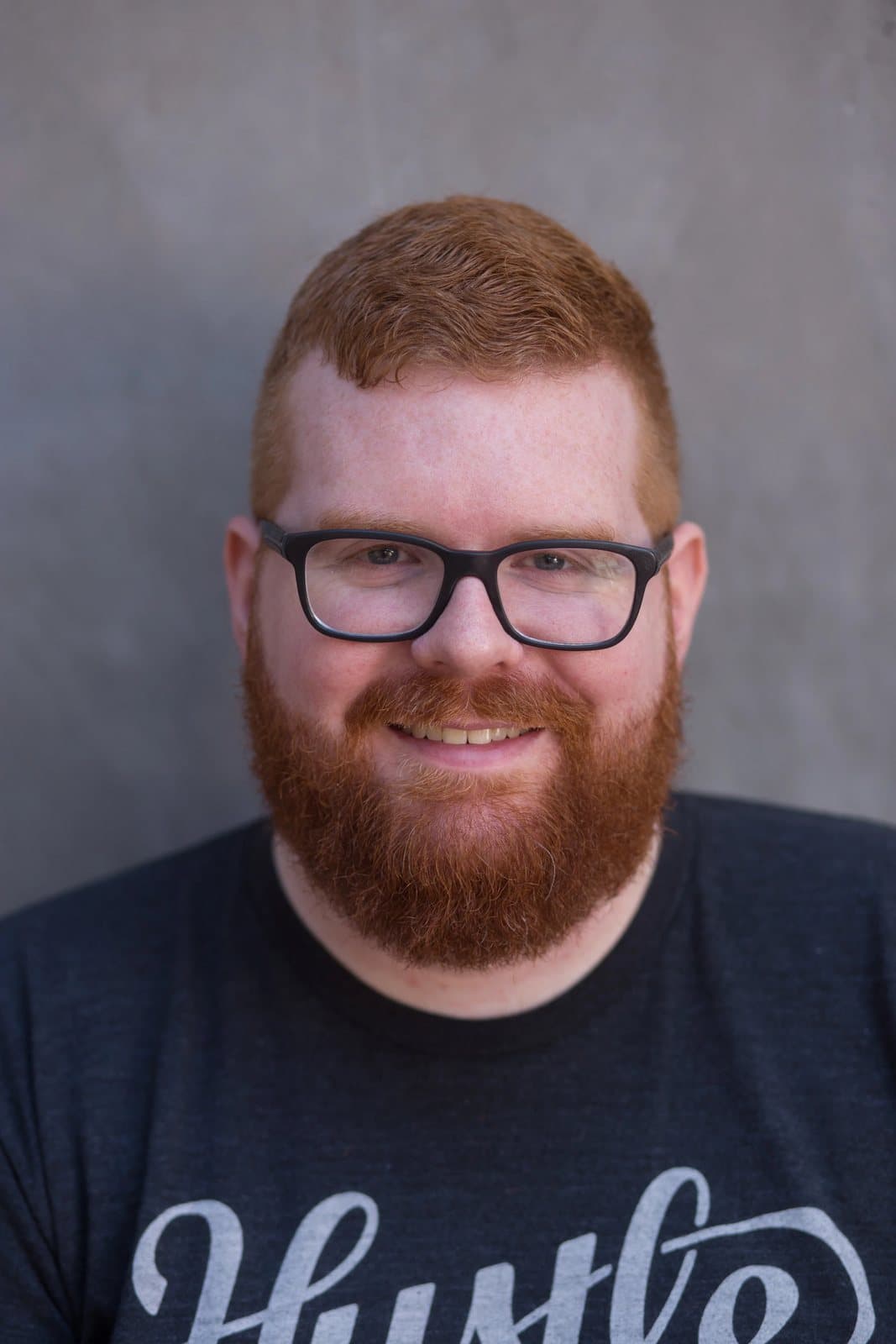 Smiling head-and-shoulders portrait of Kyle in glasses against a smooth gray wall.