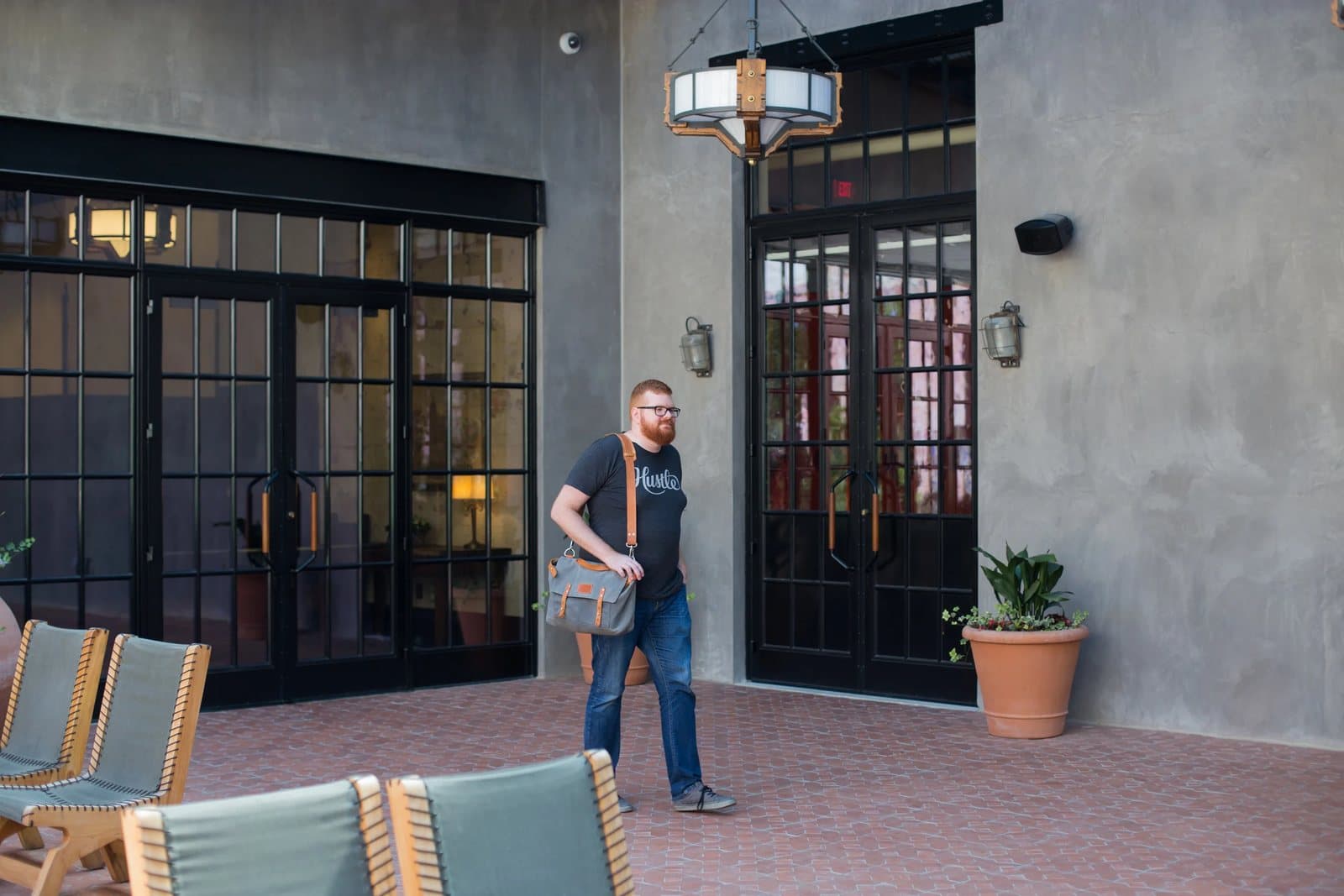 Kyle walks with a canvas messenger bag across a brick courtyard at Hotel Emma.
