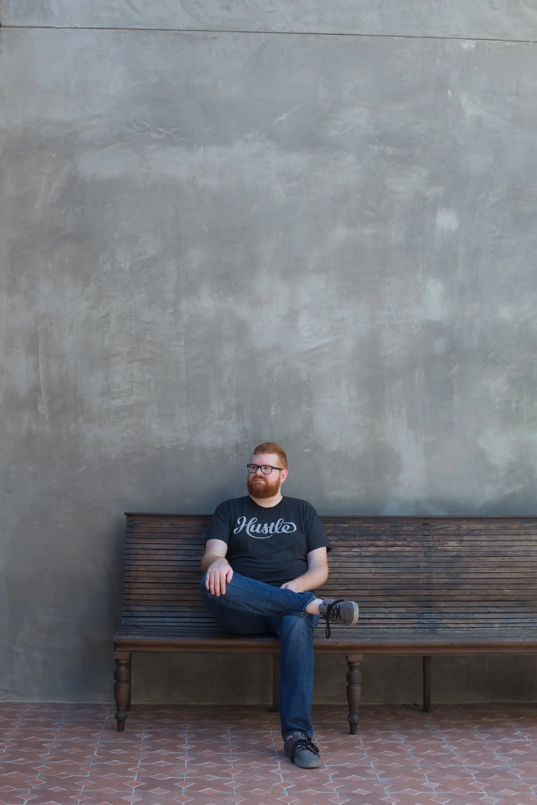 Kyle sits cross-legged on an old wooden bench against a weathered plaster wall.