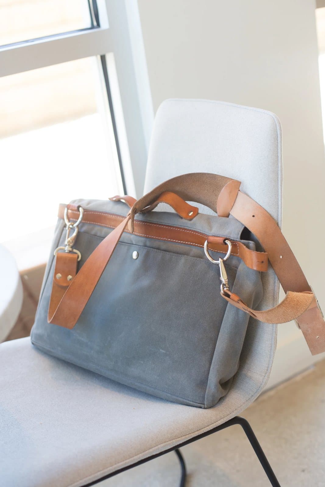 Kyle's gray canvas messenger bag with leather straps rests on a white cafe chair.