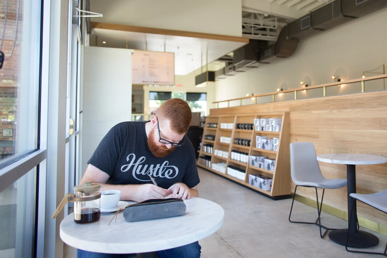 Kyle sketches at a marble table by the window of a bright, modern coffee shop.