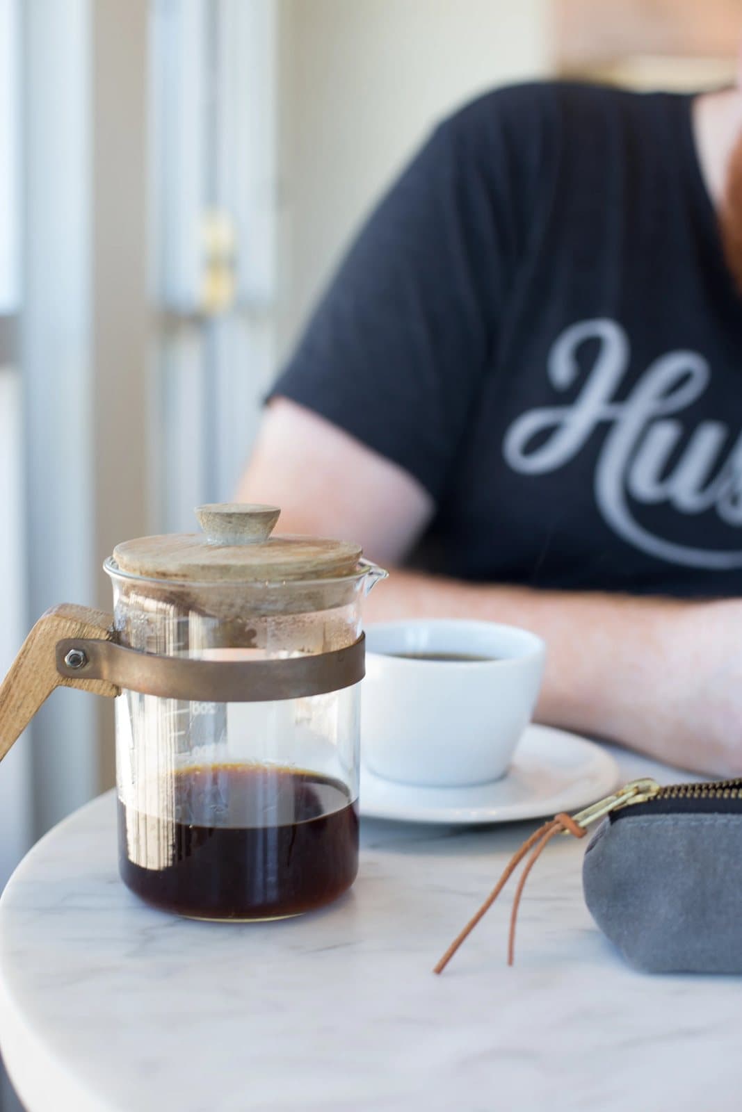 A glass French press and espresso cup on a marble table in front of Kyle at the cafe.