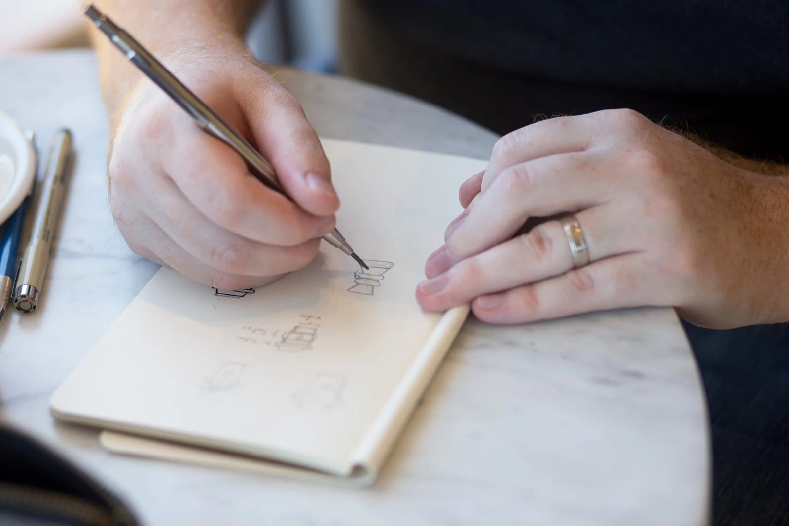 Kyle's hands draw rough icon sketches with a mechanical pencil in a small notebook.