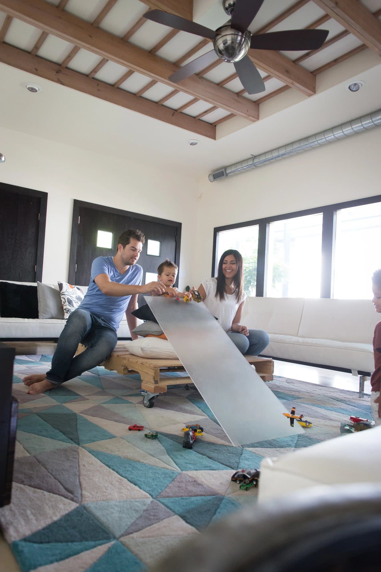 Leila and Nick race toy cars down a ramp with their boys on the living room rug.