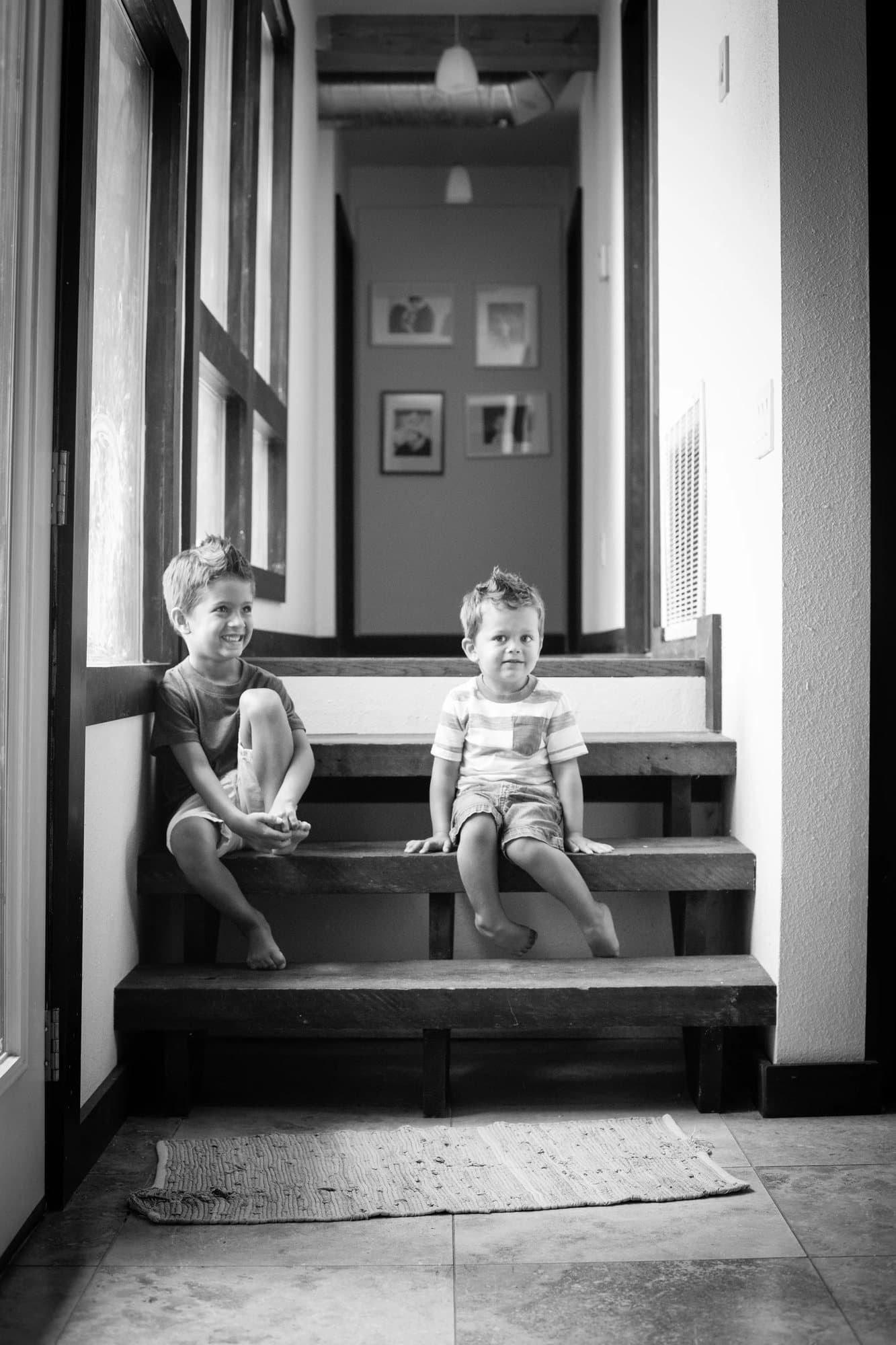Black and white shot of the two boys grinning side by side on the hallway stairs.