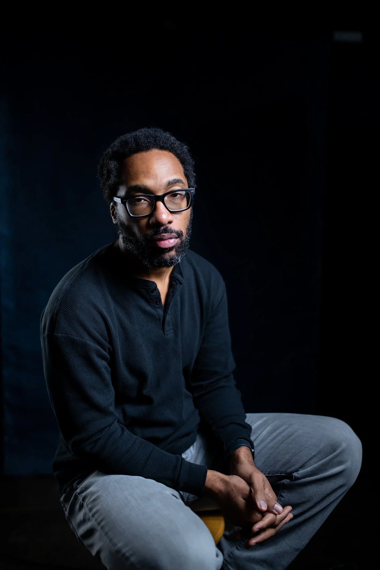 Anthony Francis, featured in Volume 35, seated in glasses and a black henley against a dark backdrop.
