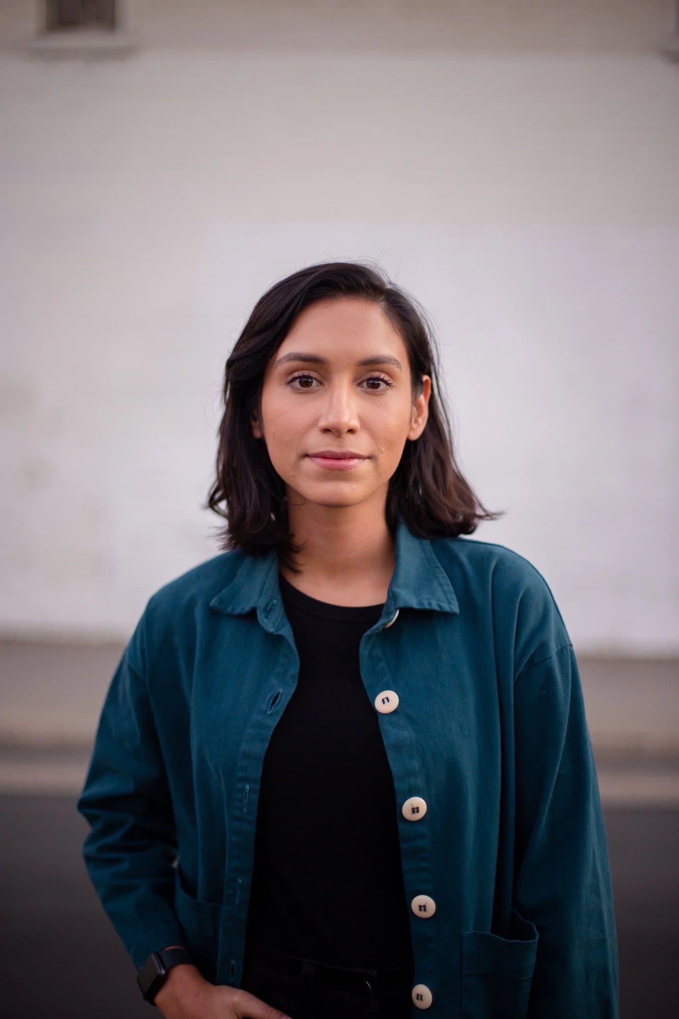 Rebekkah Cefai, featured in Volume 34, in a teal jacket against a white brick wall.