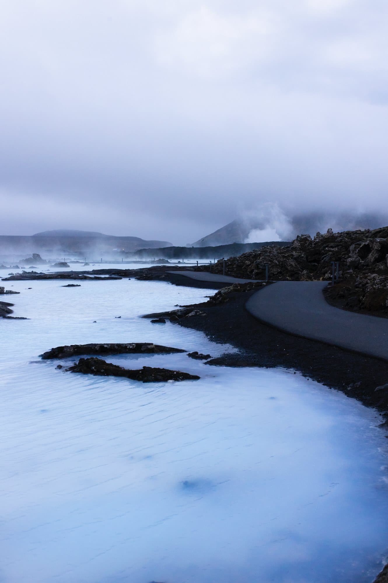 Photo handout of milky blue geothermal water and steam beside a lava rock path in Iceland.