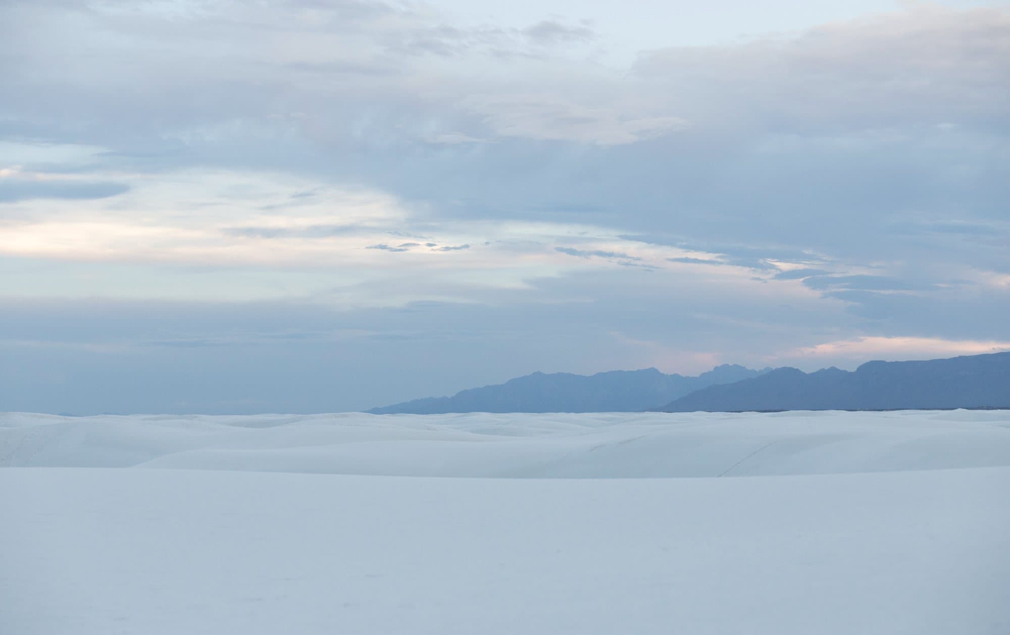 Photo handout of pale white sand dunes and distant mountains under a soft blue sky.