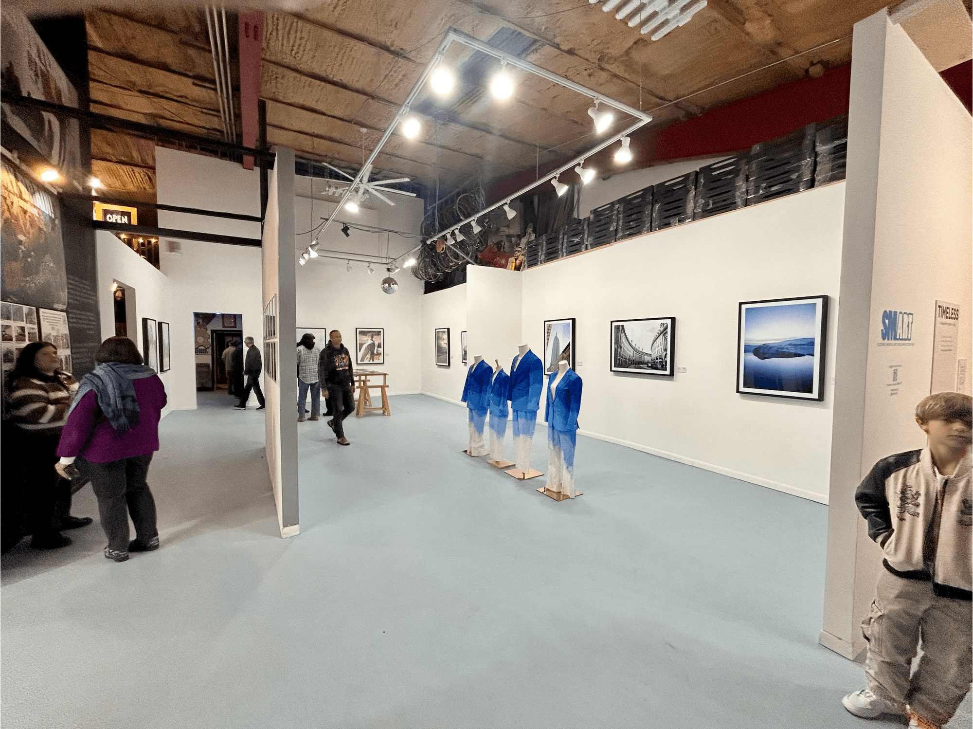 TIMELESS exhibit at 1906 Gallery, with four blue ombre suits on mannequins among framed landscape prints.