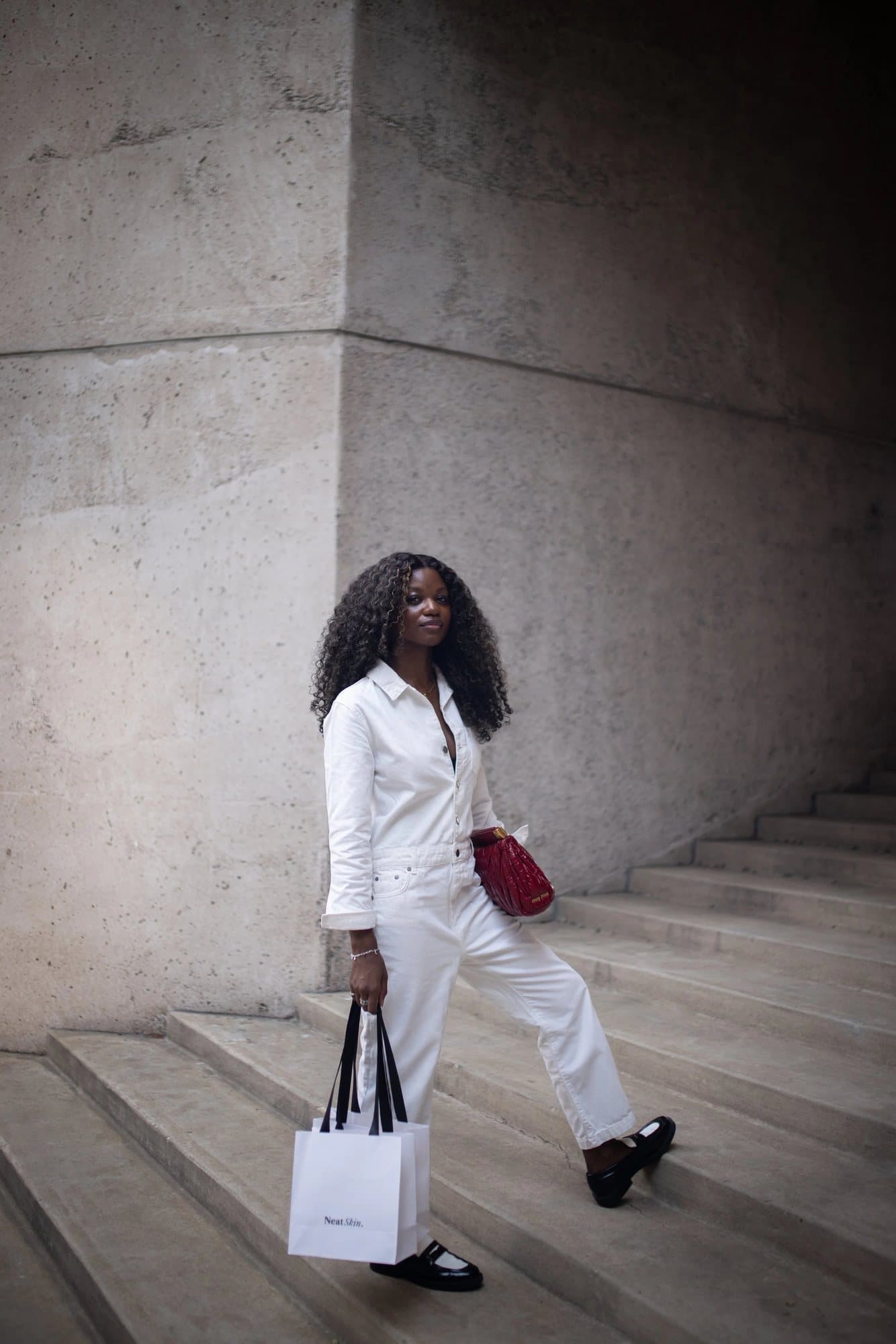 Zola-Ludivine Luvualo, featured in Volume 38, in a white jumpsuit with a red bag on stone steps.