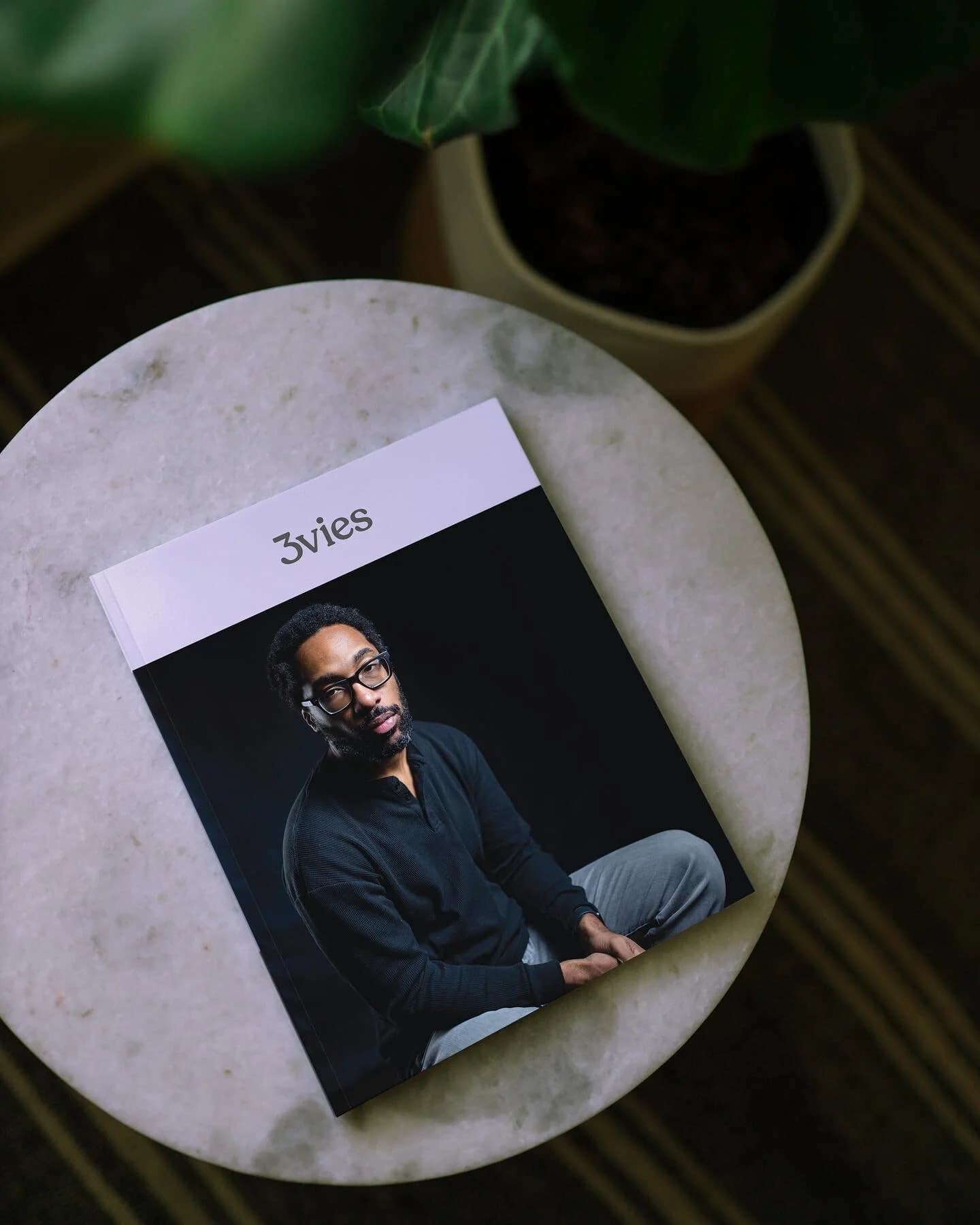 Instagram preview of Volume 35 lying on a round marble table beside a potted plant.