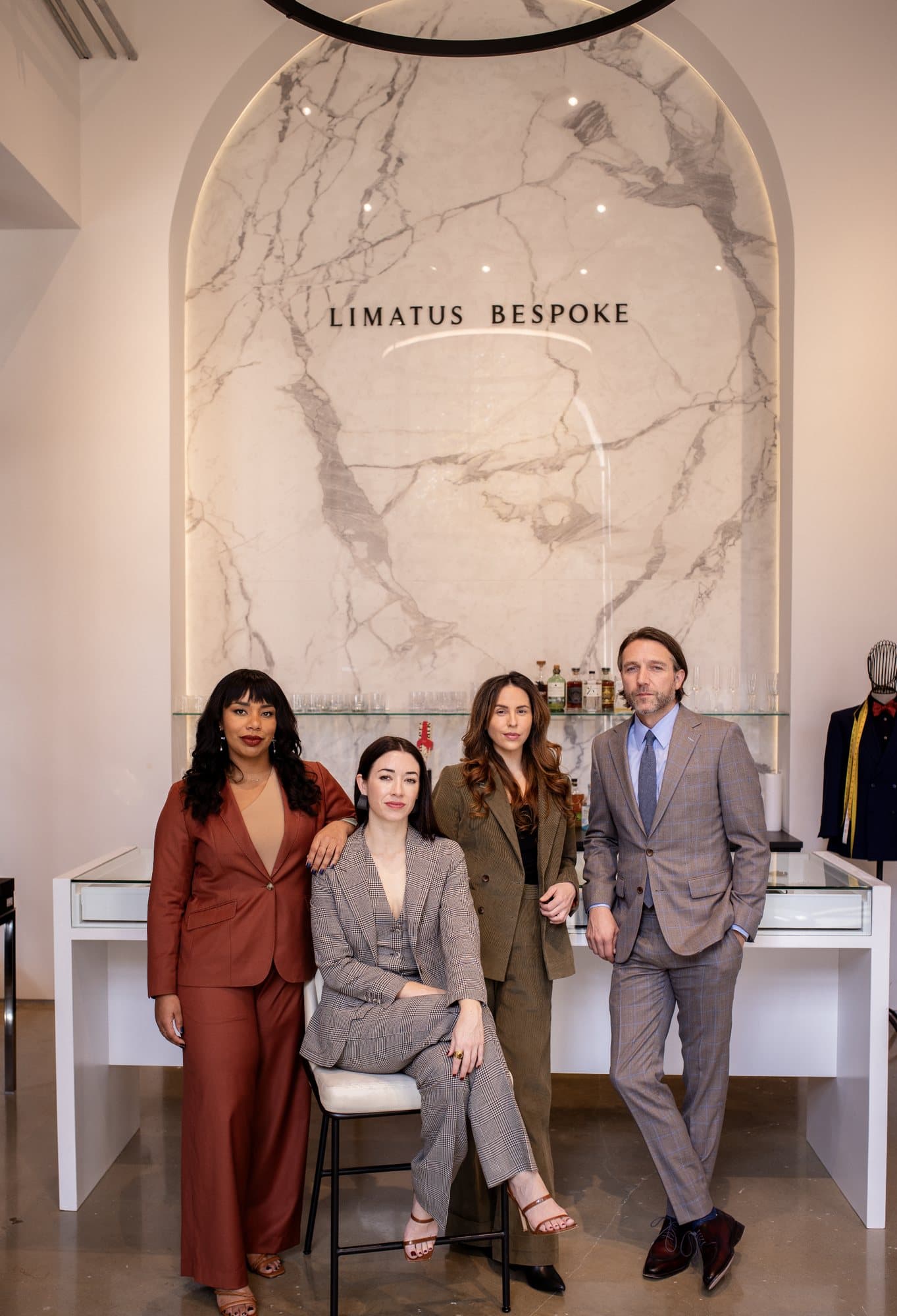 The Limatus Bespoke team in tailored suits before the marble wall bearing the brand's name.