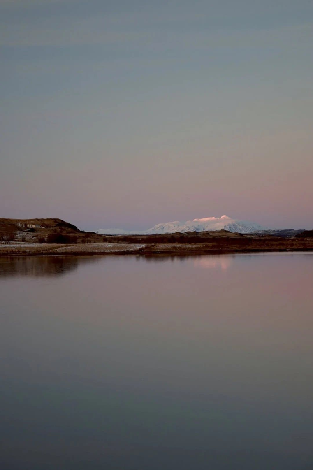 A still lake reflecting a snowy mountain under a pink dusk sky in Iceland.