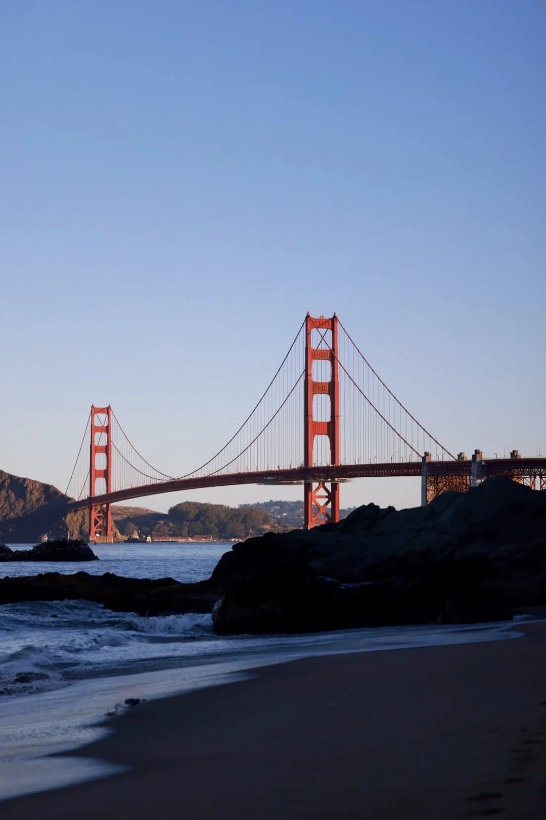 The Golden Gate Bridge seen from a rocky San Francisco beach in late afternoon light.