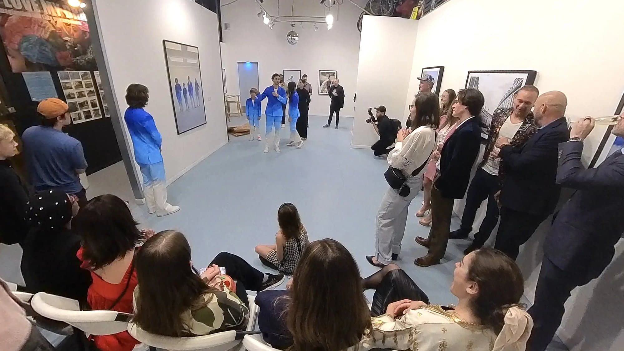 Guests gather in the gallery at the Timeless opening as Mark and his children, in blue painted suits, address the crowd.