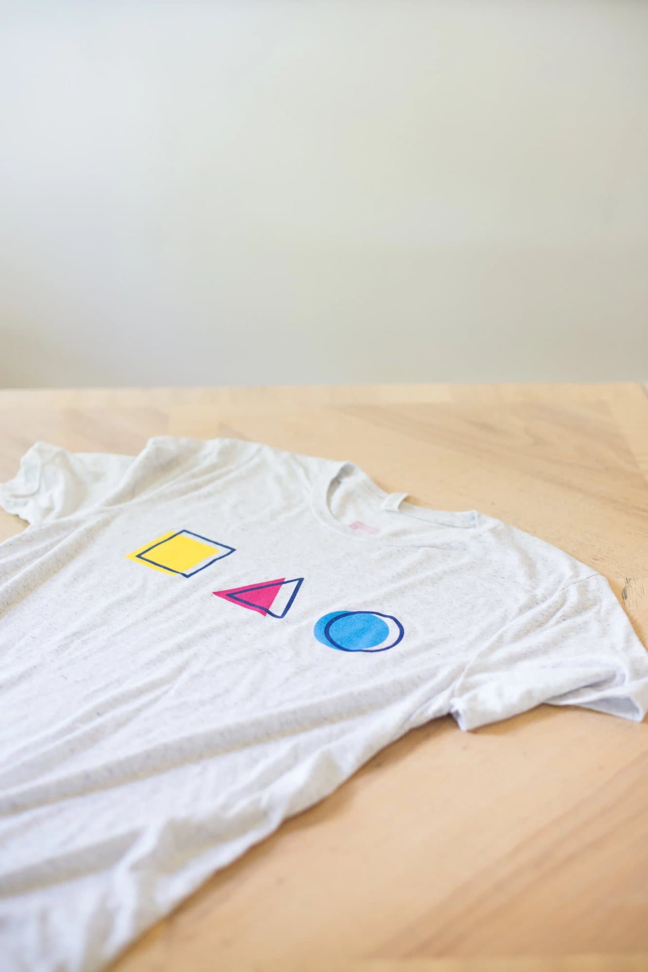 A heather white WW@SA 2017 shirt printed with a yellow square, pink triangle, and blue circle.