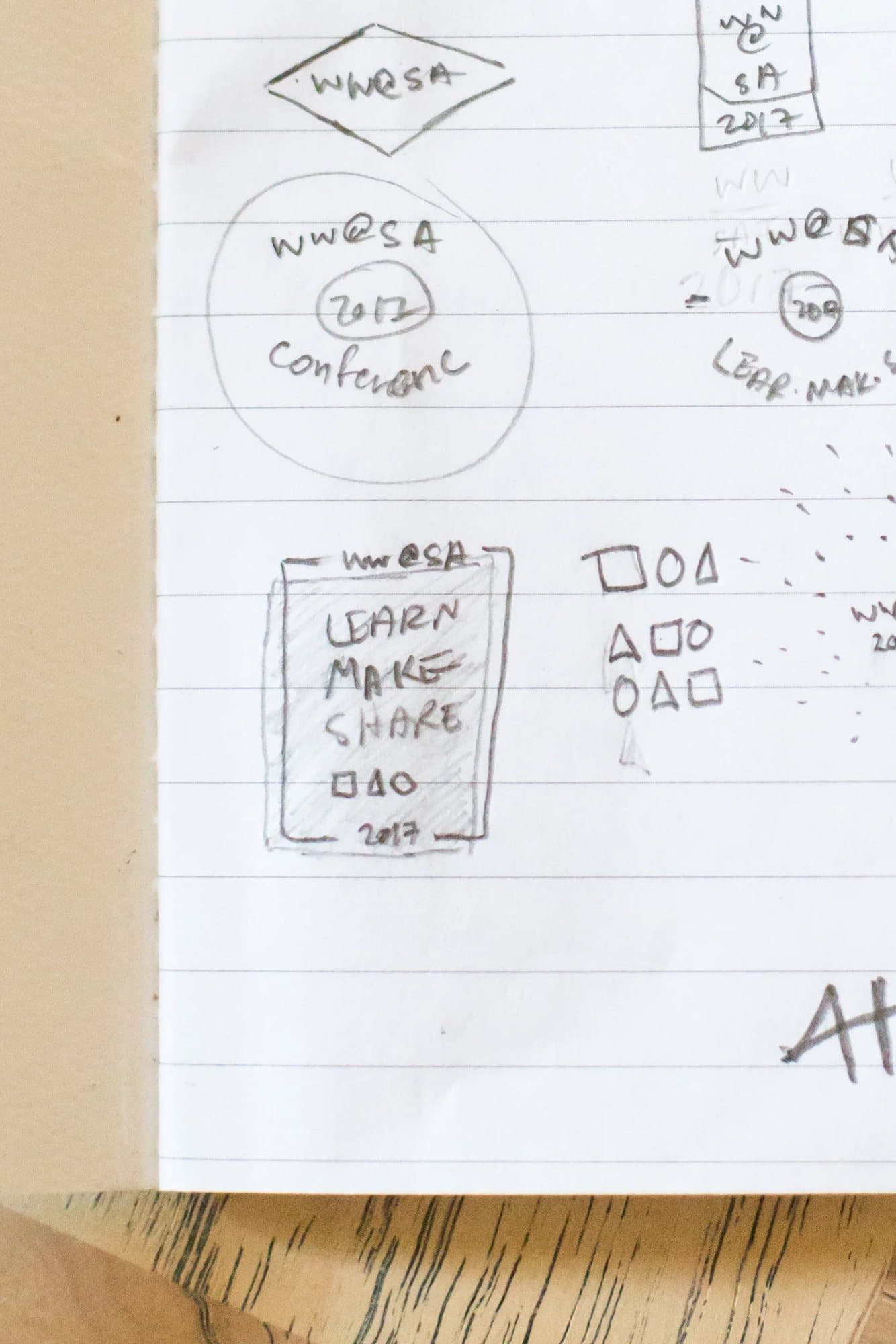 Close view of pencil sketches of WW@SA badges, a Learn Make Share card, and the three shapes.